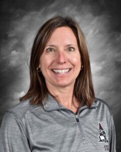 Smiling woman with shoulder-length brown hair, wearing a gray pullover, against a gray backdrop.