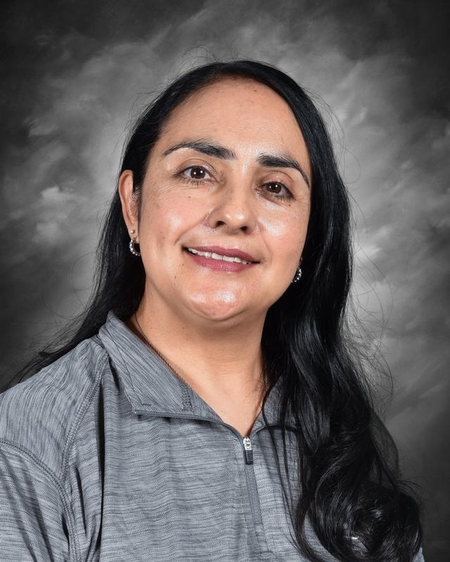 A woman with long black hair smiles, wearing a gray zip-up shirt, against a soft gray background.