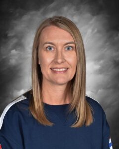 Portrait of a woman with long blonde hair, wearing a dark blue sweatshirt, smiling against a gray background.