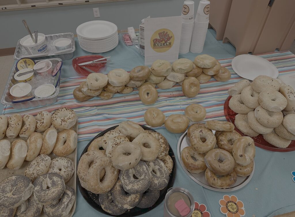 A table spread with various bagels, cream cheese, plates, and cups for a bagel breakfast event.