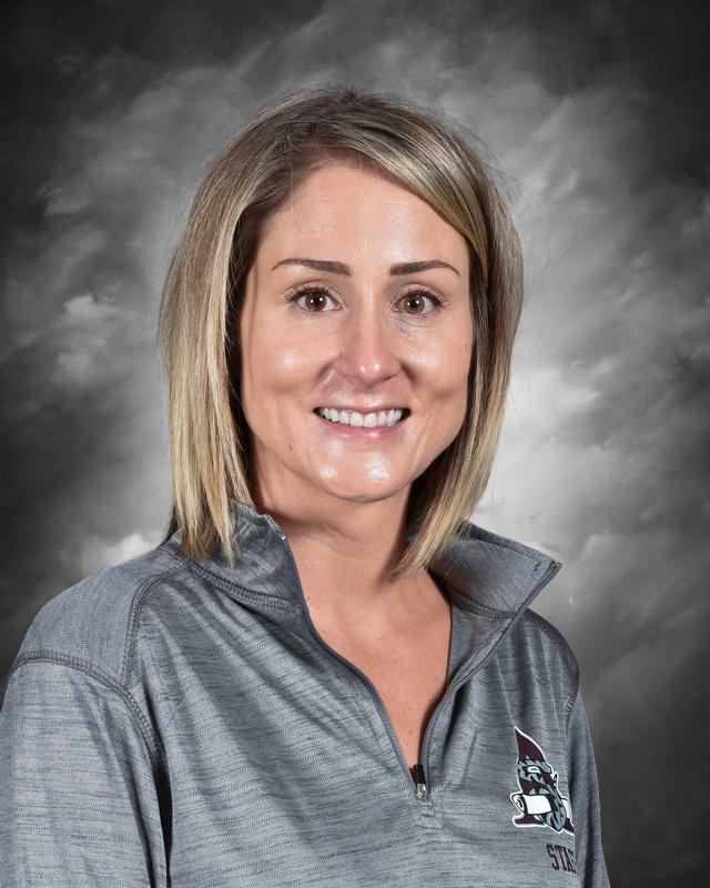 Smiling woman with shoulder-length blonde hair, wearing a gray zip-up shirt, against a gray background.