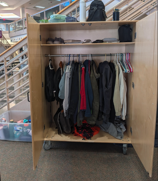 A lost and found cabinet displaying various jackets and hoodies hanging on hangers, and bags on shelves above.