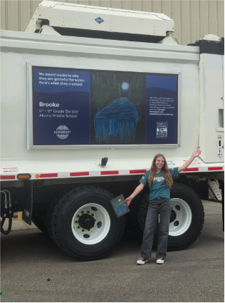 A student stands next to a truck featuring her artwork and name, showcasing a project about gratitude.